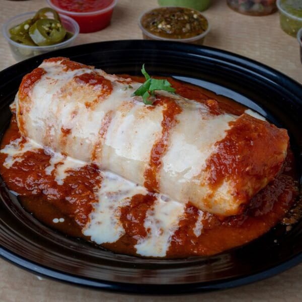 A large, saucy Uncle Berto's Burrito covered in red and white sauce, garnished with cilantro.