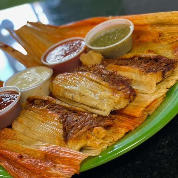 Three Uncle Berto's tamales with shredded meat filling, served with four small sauce cups on a green plate.