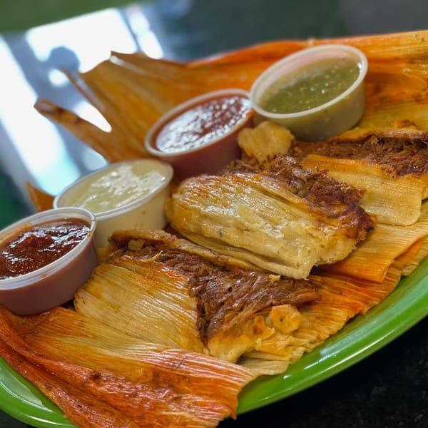 Tamales with shredded meat, served on a green plate with four small cups of salsa.