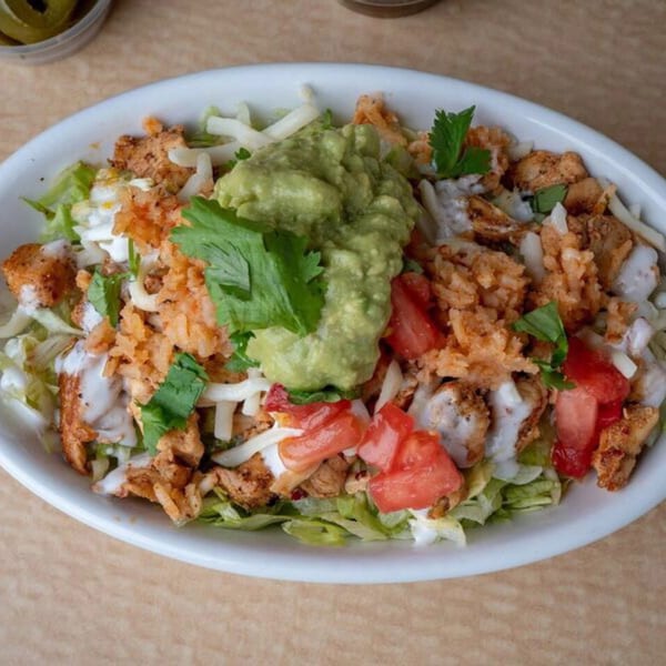 A Mexican chicken salad bowl with lettuce, rice, tomatoes, cheese, and guacamole.