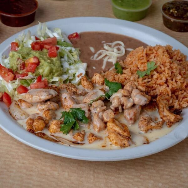 A Mexican dish with chicken in cream sauce, rice, refried beans, guacamole, and shredded lettuce.
