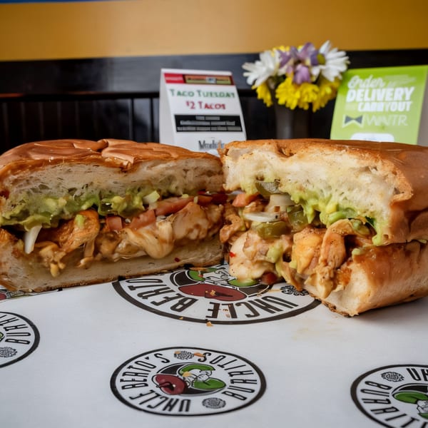 A large Uncle Berto's Burritos torta, cut in half, filled with chicken, guacamole, and vegetables.