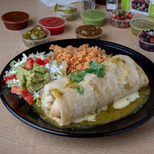 A large Uncle Berto's Burritos meal with a green chile burrito, rice, salad, and various salsas.