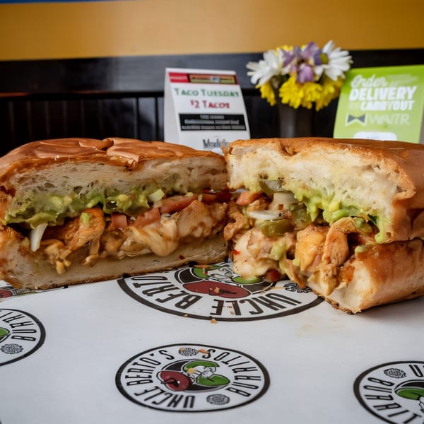 A large Uncle Berto's Burritos sandwich, cut in half, filled with chicken, guacamole, and vegetables.